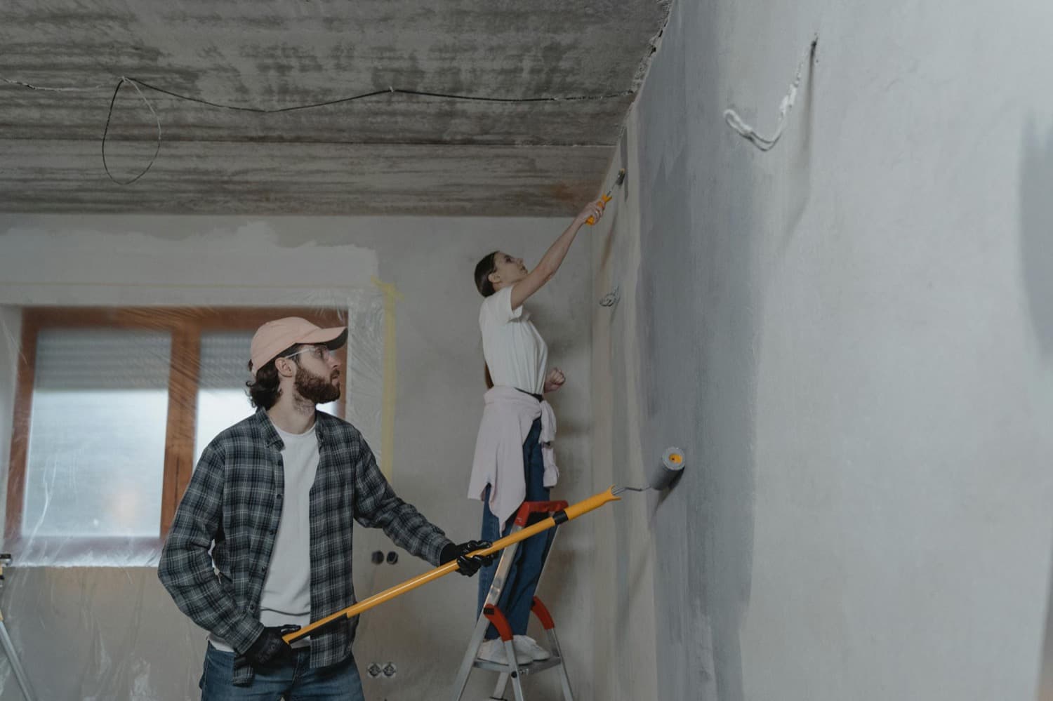 Couple rénovant l'intérieur de sa maison, rouleau et échelle à la main